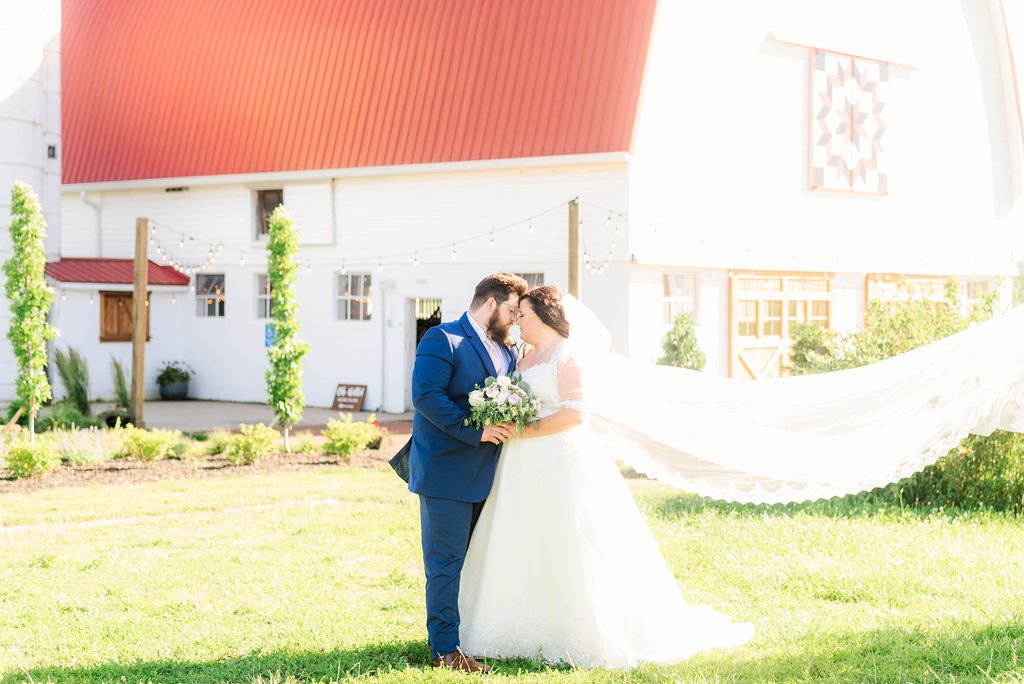 A couple beneath a veil beside the white barn.