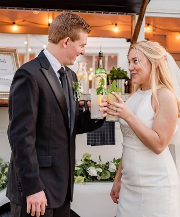 A couple toasting cocktails at the bar under the string lights.