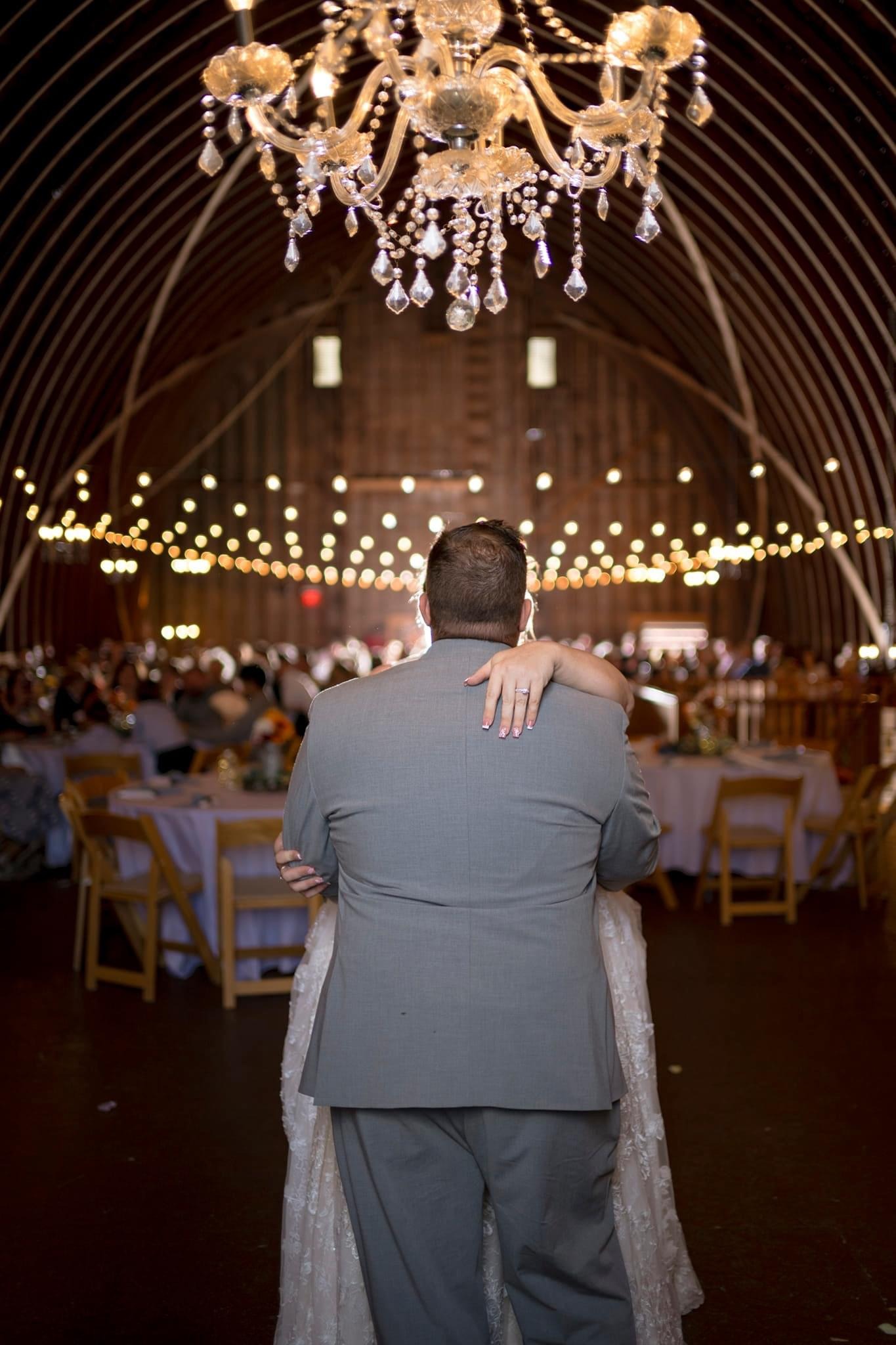 A couple dancing under the chandelier with the barn full behind them.