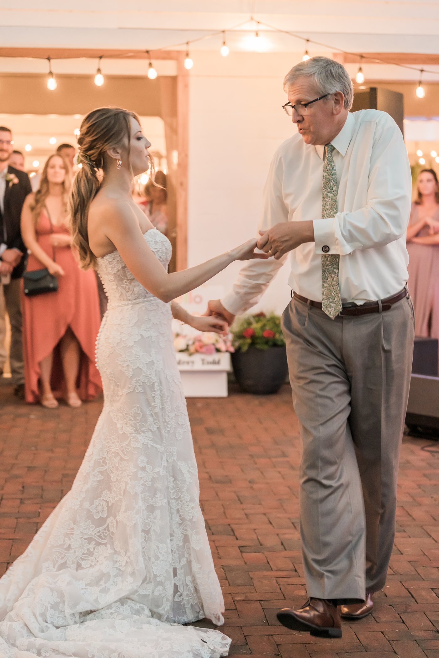 A father and daughter dance together beneath the string lights.