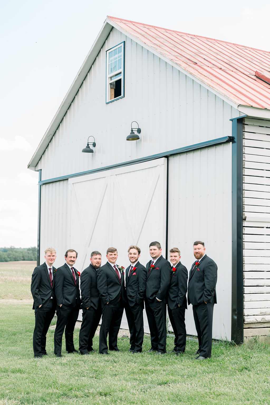 Groomsmen lined up outside the white corn crib with its red roof.