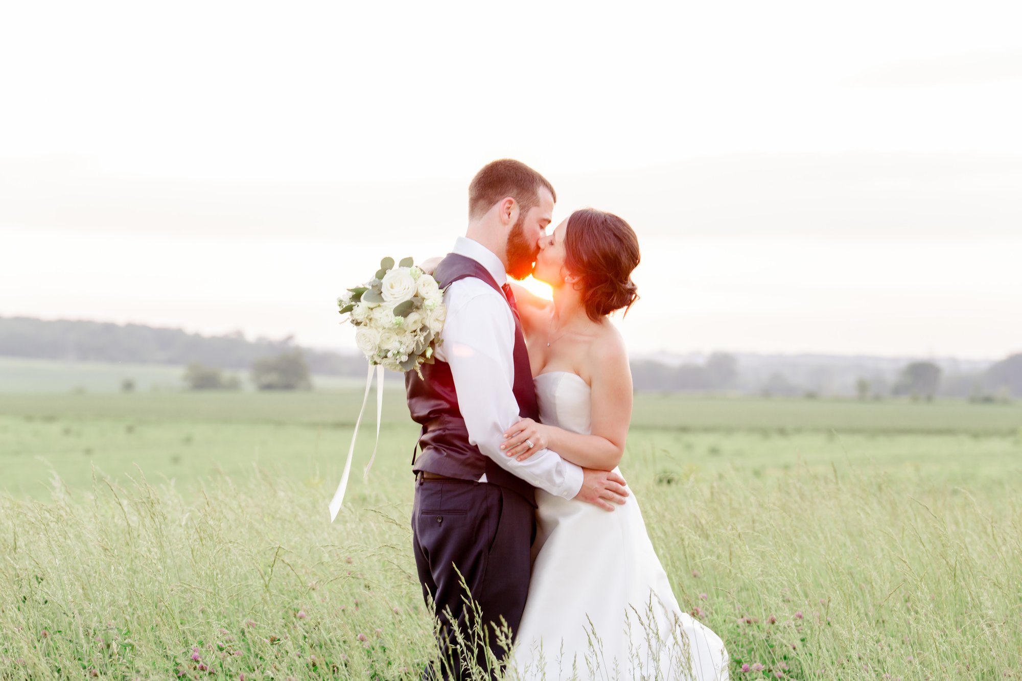 Couple kissing in tall grass at sundown.