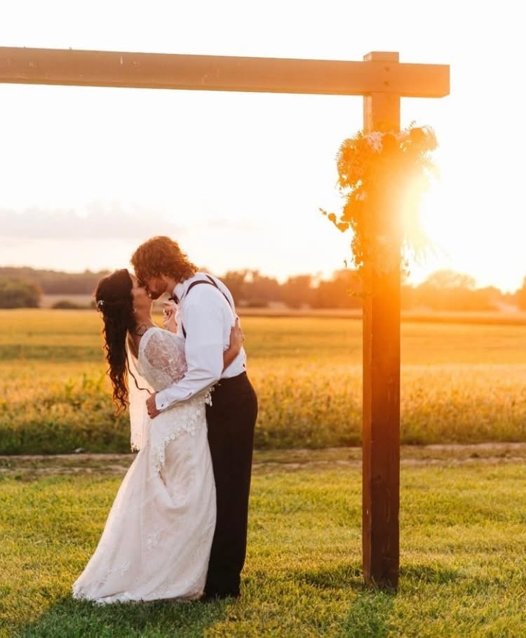 A couple together by the fence post as the sun goes down behind the field.