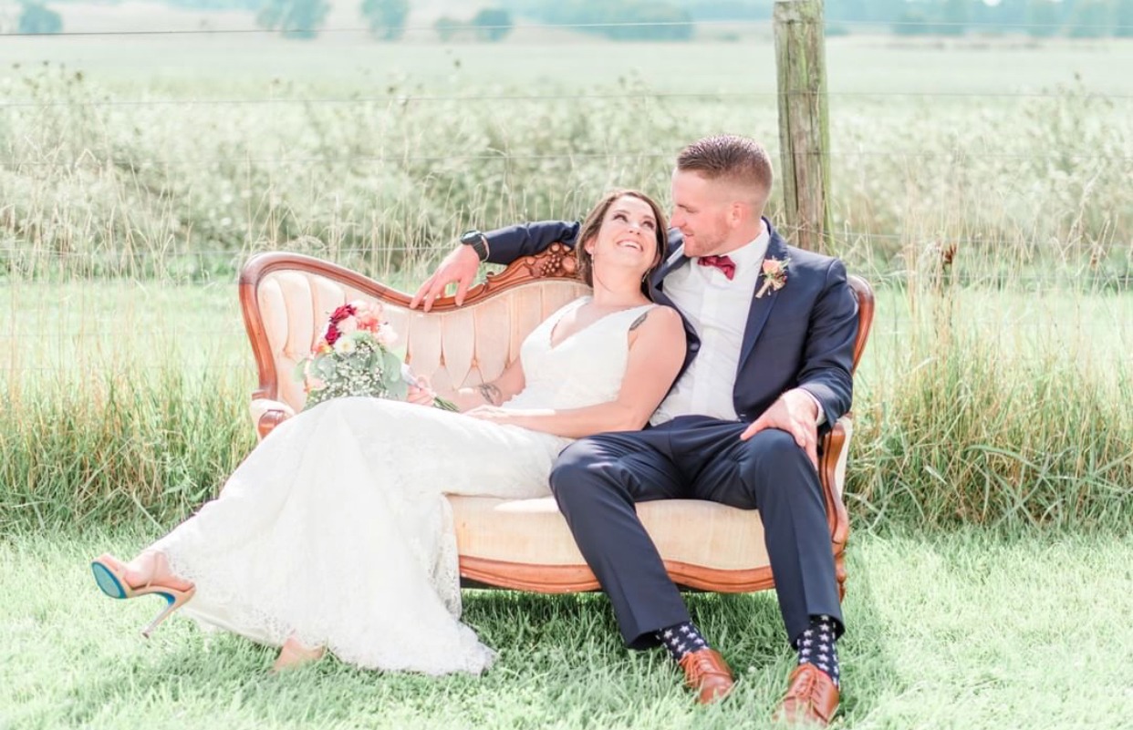 A couple sitting together on a vintage sofa out in the open field.