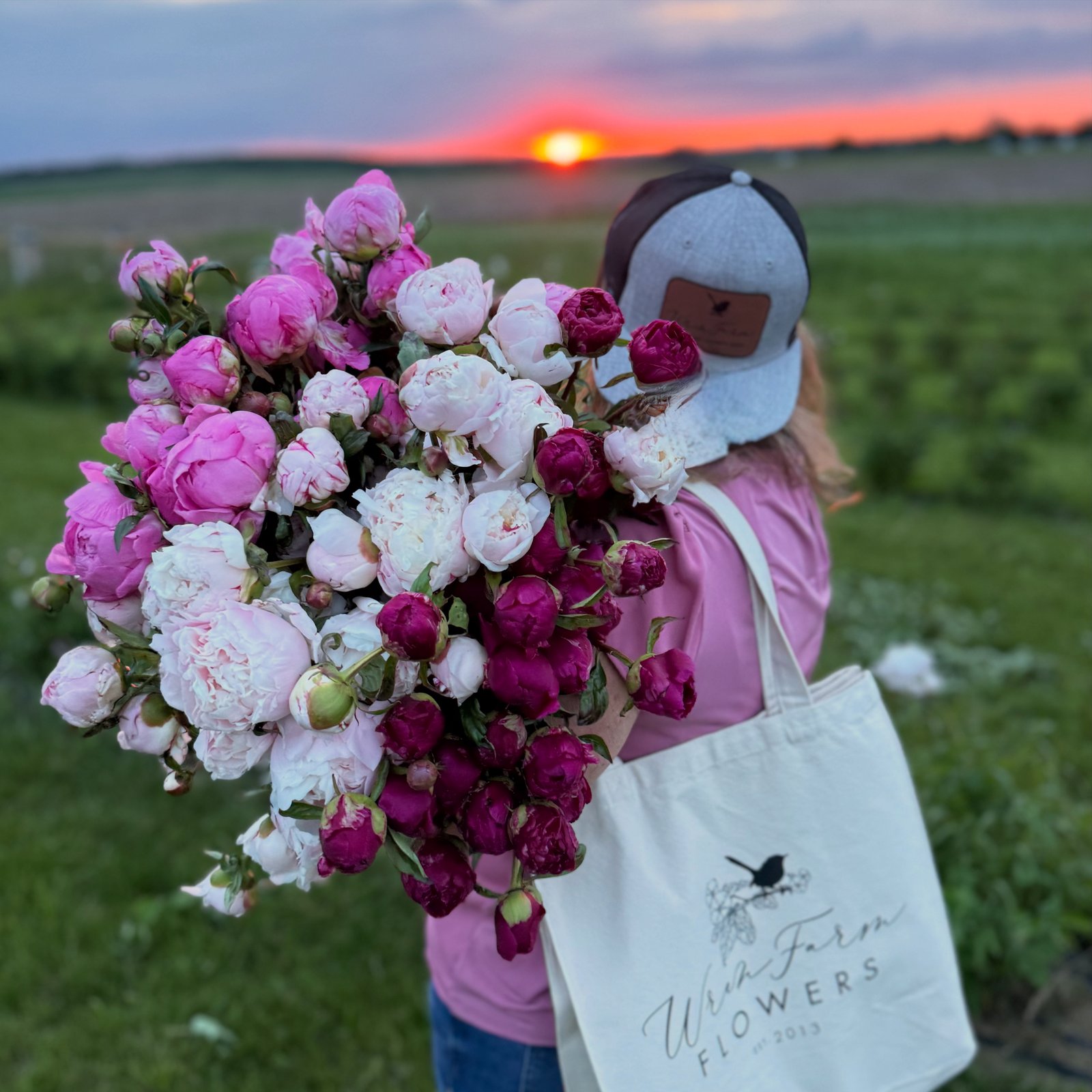 An armful of peonies and the Wren Farm Flowers tote against a red sunset.