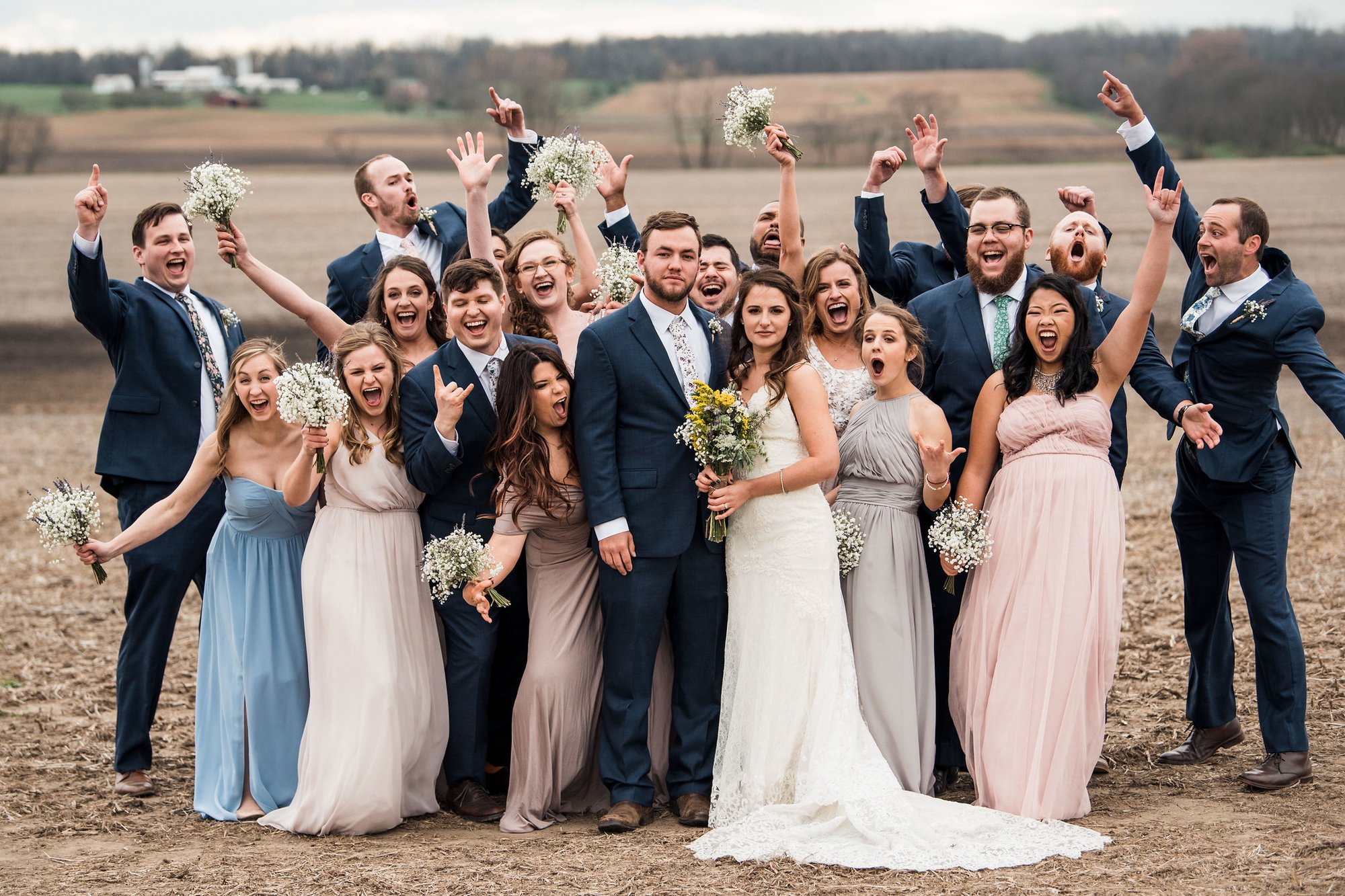 Wedding party cheering around the couple in a harvested field.