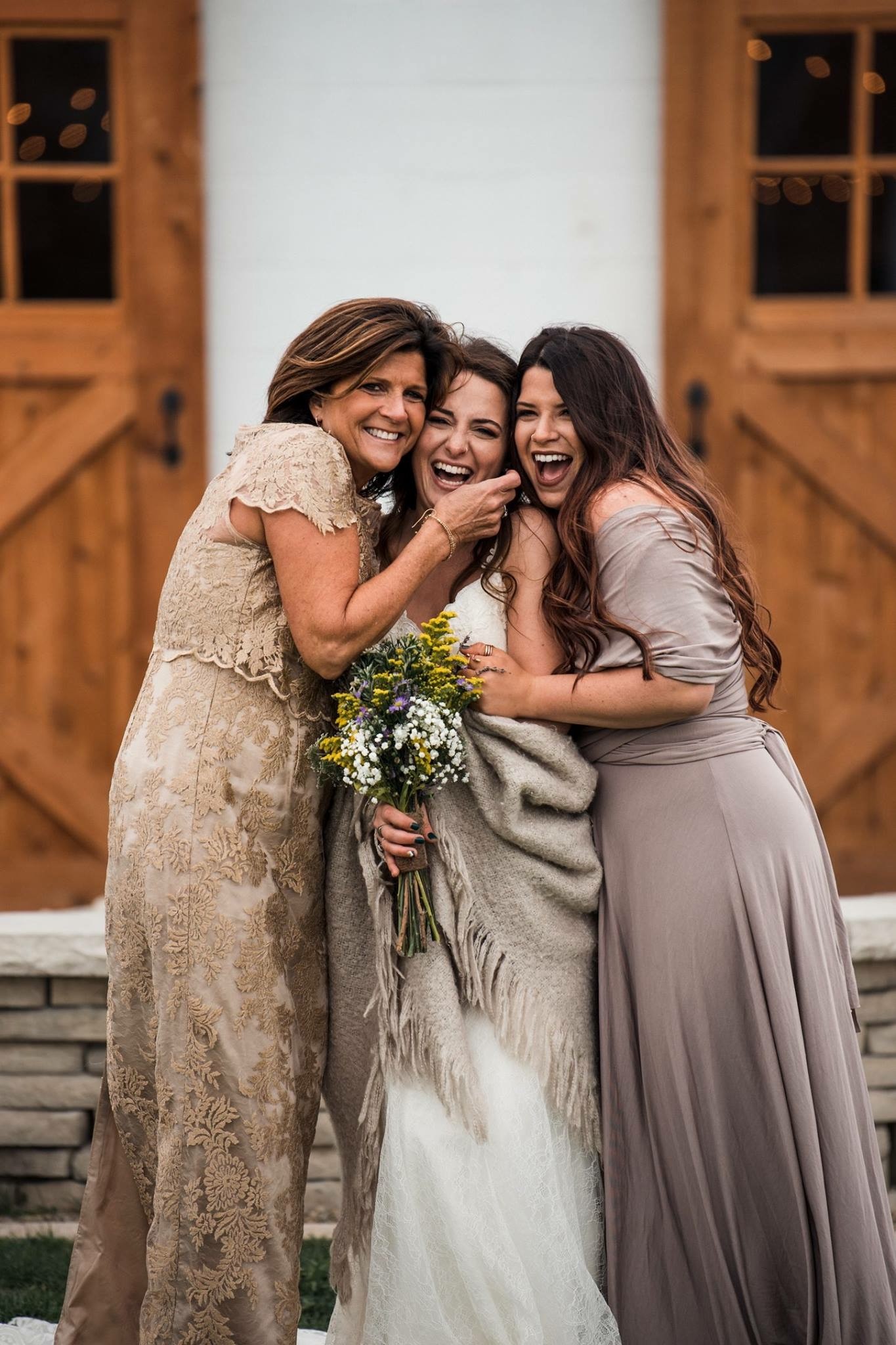 Three of the wedding party laughing together by the open barn doors.
